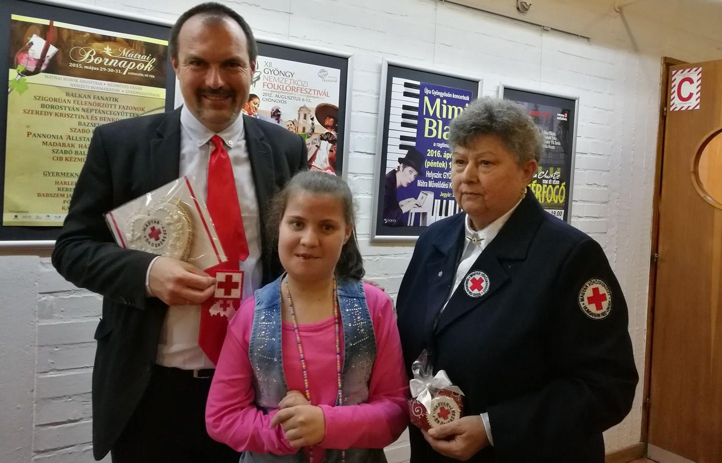 Virág gyógyíthatatlan beteg, fél oldalára lebénulva éli mindennapjait. Ennek ellenére hatalmas szívvel van megáldva, hiszen mindenképpen szeretett volna adni egy apró ajándékot azoknak, akik rendszeresen, önzetlenül ajánlják fel a vérüket egy számukra ismeretleneknek. Elhatározta tehát, hogy hálája jeléül egy kézzel készített vöröskereszt-szimbólumot fog adni ezeknek a véradóknak. A kislány 150 darab kis piros-fehér keresztes kabalát készített, amelyet a Gyöngyösi Véradók Ünnepén vehettek át az illetékesek